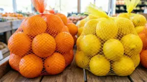 Confezioni di arance in rete arancione e limoni in rete gialla su un banco di frutta al supermercato