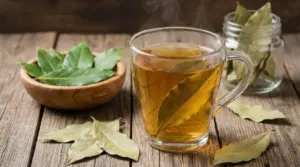 Tazza di tisana all’alloro fumante su tavolo di legno, con foglie di alloro fresche e secche accanto