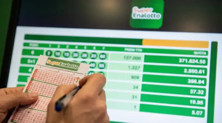 Mano che compila una schedina del SuperEnalotto davanti a uno schermo con risultati e quote della vincita